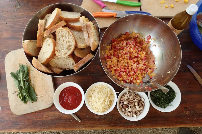 Zubereitung von Pizzabrötchen. Aufgeschnittenes Weißbrot, Belag und Zutaten wie Käse und Kräuter